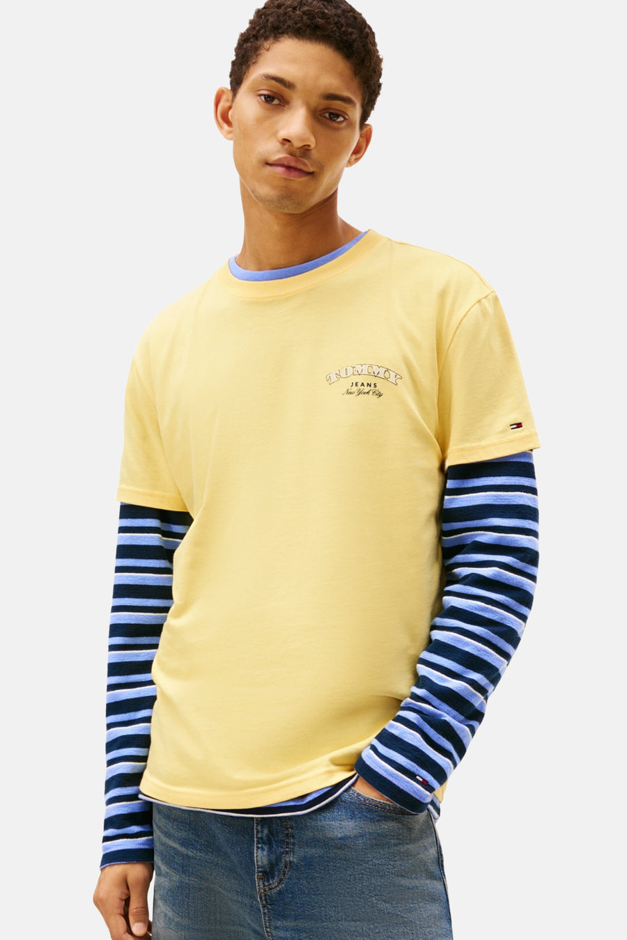 Jonge man draagt gele T-shirt met lange mouwen met blauwe strepen en blauwe spijkerbroek.