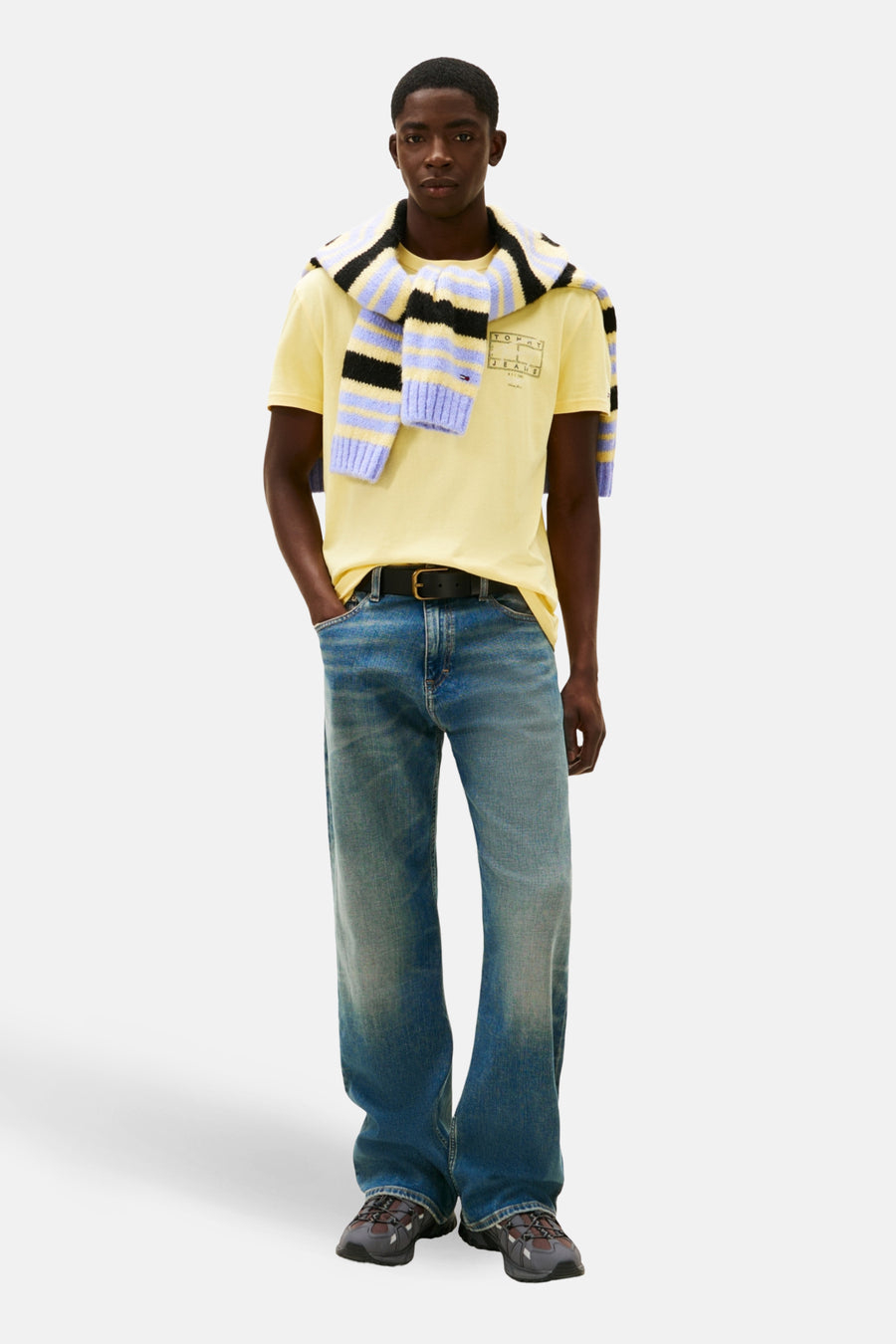 Man in gele T-shirt met gestreepte trui, jeans en wandelschoenen.