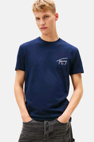 T-shirt bleu à manches courtes de TOMMY JEANS, avec une impression graphique sur le dos, associé à un jean foncé.