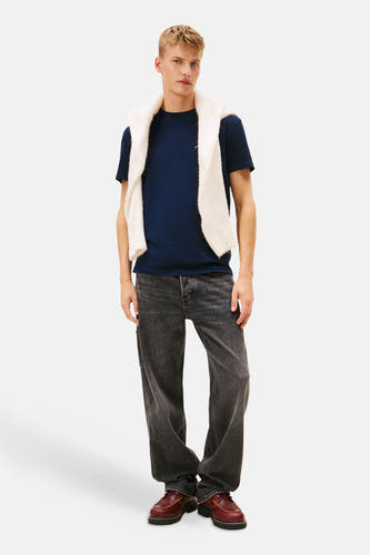 T-shirt bleu à manches courtes de TOMMY JEANS, avec un pull blanc décontracté sur les épaules.