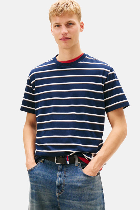 Man met blond haar draagt blauw-wit gestreept shirt en jeans, handen in de zakken.