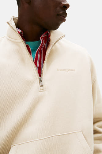 Gilet beige de TOMMY JEANS avec fermeture à glissière sur et col rayé rouge sur un T-shirt turquoise.