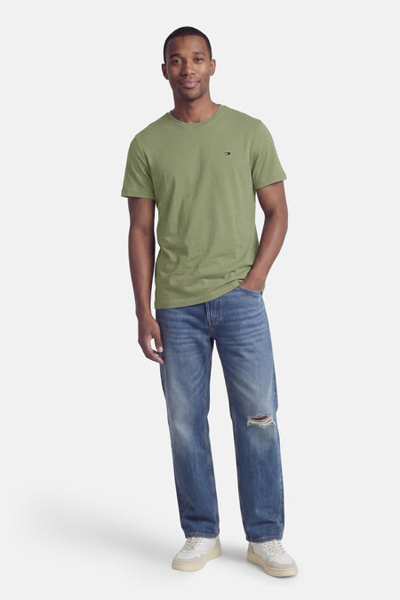 Groene korte mouw T-shirt van TOMMY JEANS, ronde hals, klein logo op borst, model in lifestyle pose met spijkerbroek en witte sneakers
