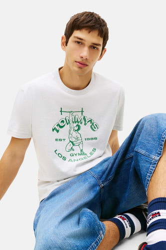 T-shirt gris à manches courtes de TOMMY JEANS, avec imprimé de baskets vertes et d'un jean bleu.