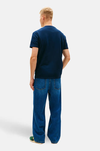 T-shirt bleu à manches courtes de TOMMY JEANS, vu de dos, associé à un jean ample et des chaussures vertes.