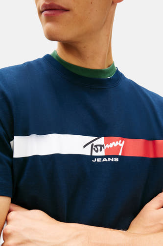 T-shirt bleu à manches courtes de TOMMY JEANS, avec une bande horizontale blanche et rouge sur la poitrine.