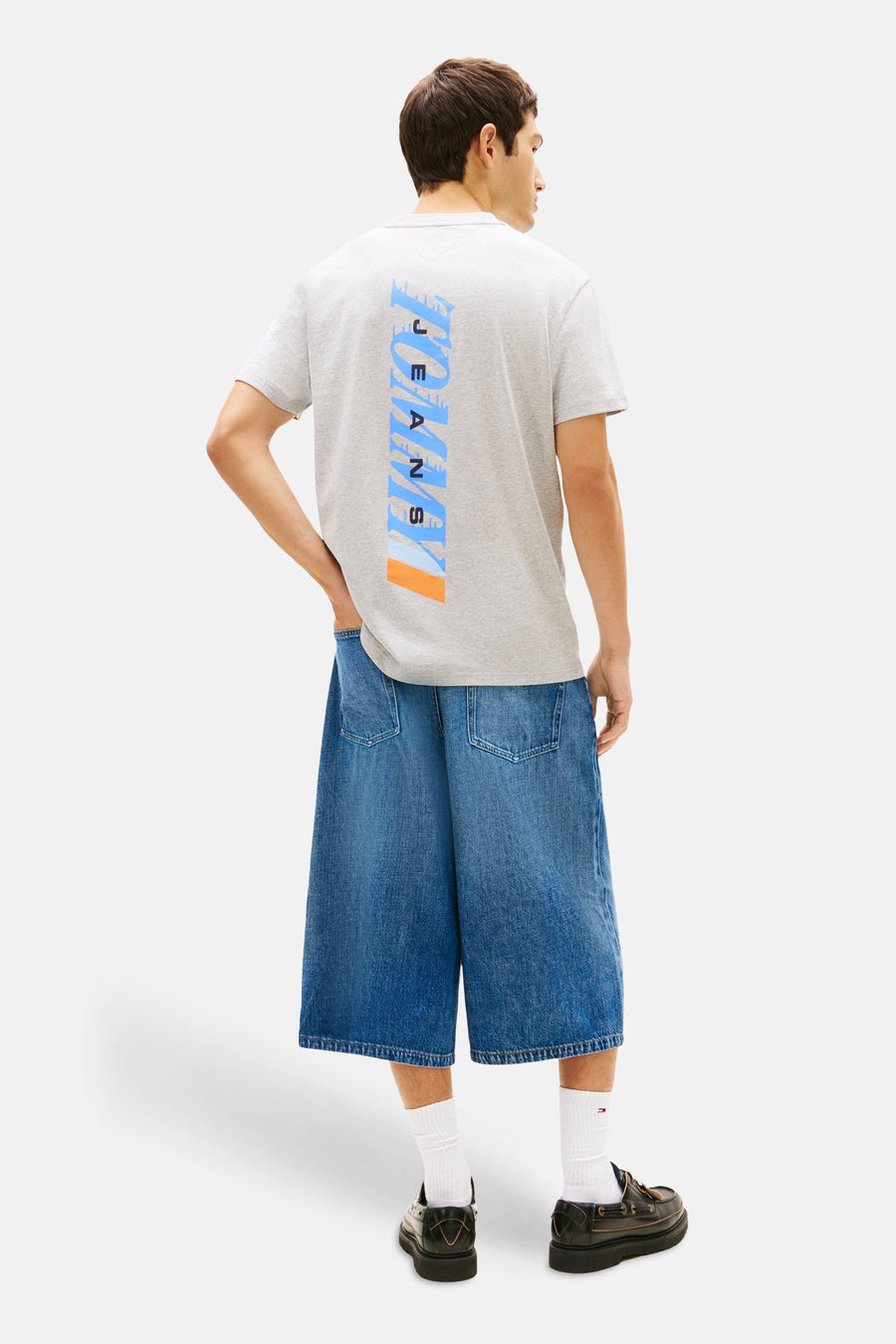 T-shirt gris à manches courtes de TOMMY JEANS, avec inscription verticale du logo dans le dos et associé à un short en jean ample.