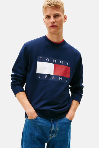 Pull-over bleu de TOMMY JEANS, vu de de derrière, avec des jeans larges et des baskets blanches.