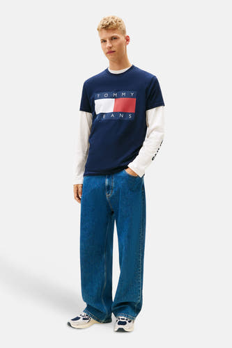 T-shirt bleu à manches courtes de TOMMY JEANS, porté sur un t-shirt blanc à manches longues et un jeans large.
