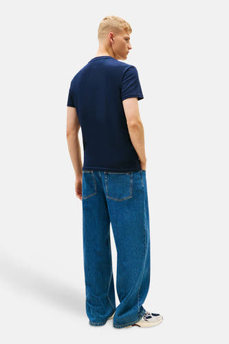 Blauw T-shirt met korte mouwen van TOMMY JEANS, gedragen met wijde jeans en sneakers.
