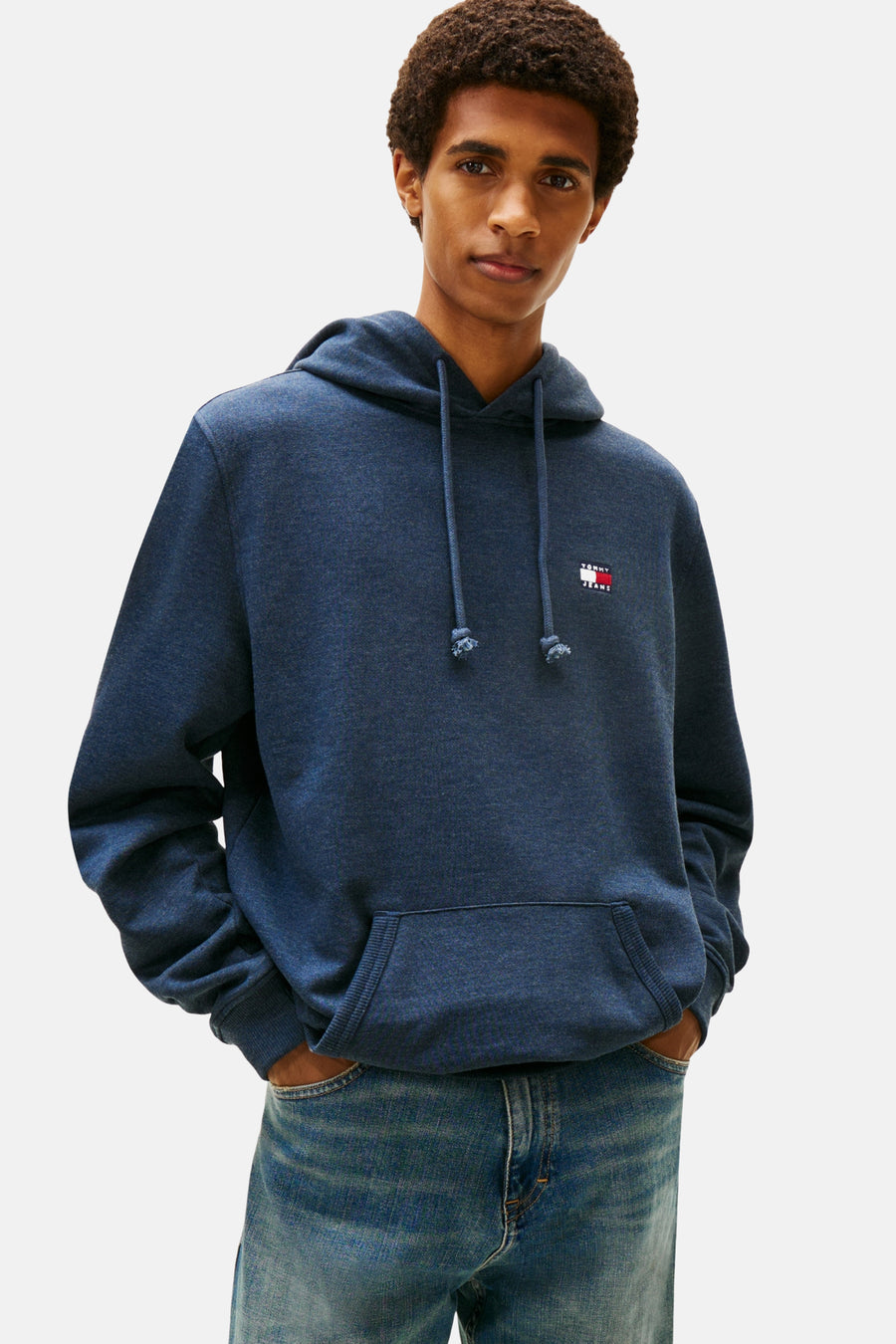 Man met blauwe hoodie met logo en jeans.