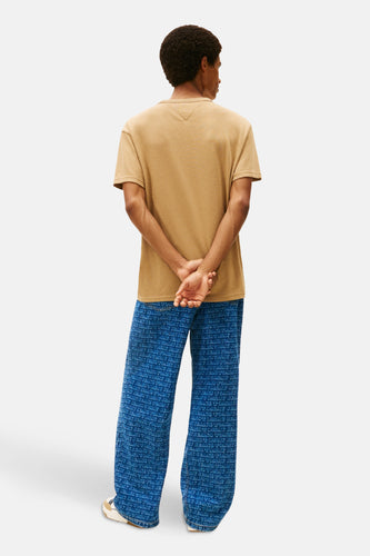 Achterkant van een man in bruin T-shirt en blauwe jeans met logo-print, staand op een witte achtergrond.