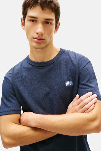 T-shirt bleu à manches courtes de TOMMY JEANS, avec des bras croisés sur la poitrine.