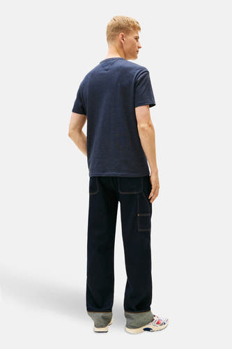T-shirt bleu à manches courtes de TOMMY JEANS, vu de dos avec un pantalon foncé et des baskets colorées.