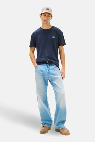 T-shirt bleu à manches courtes de TOMMY JEANS, avec petit logo sur la poitrine, associé à des jeans, une ceinture et un chapeau.
