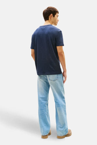 T-shirt bleu à manches courtes de TOMMY JEANS, vu de dos, avec des jeans bleus clairs et des chaussures marrons.