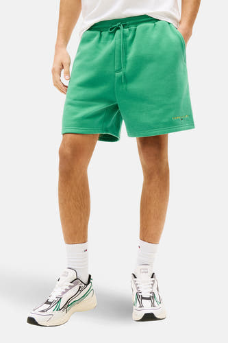 Short vert TOMMY JEANS, combiné avec un t-shirt blanc à logo et des baskets blanches à accents verts.