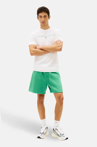 Groene short van TOMMY JEANS, gecombineerd met een wit T-shirt met logo en witte sneakers met groene accenten.
