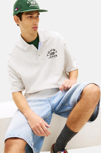 Polo grise à manches courtes de TOMMY JEANS, avec logo sur la poitrine, porté avec un haut vert et un short en jean.