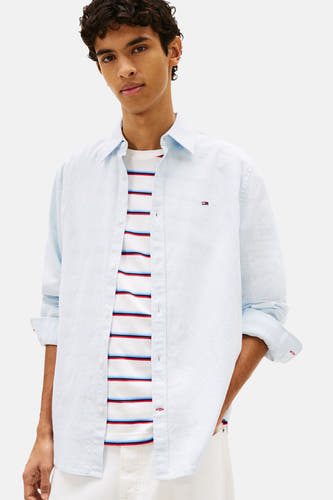 Chemise bleue de TOMMY JEANS, portée sur un haut rayé, avec un pantalon blanc et une casquette bleue.