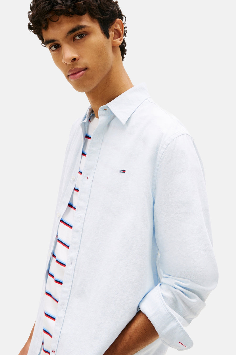 Chemise bleue à manches longues de TOMMY JEANS, portée sur un t-shirt rayé.