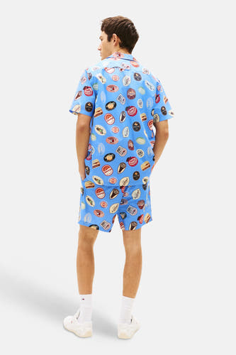 Chemise bleue à manches courtes Tommy Jeans, ornée d'un motif badge rétro et portée avec un short assorti.