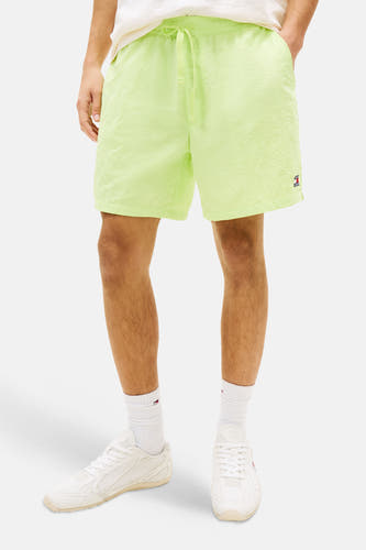 Short jaune de TOMMY JEANS, porté par un homme avec un T-shirt de couleur crème et des baskets blanches.