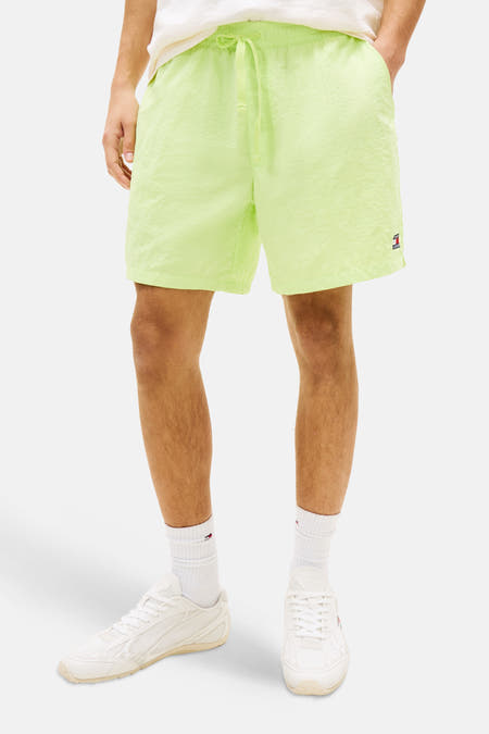 Short jaune de TOMMY JEANS, porté par un homme avec un T-shirt de couleur crème et des baskets blanches.