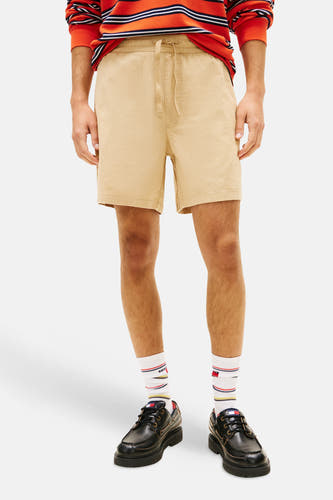 Short marron avec cordon de serrage de TOMMY JEANS, porté avec un polo orange rayé, des chaussettes blanches et des chaussures noires.