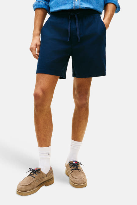 Short bleu de TOMMY JEANS, combiné avec une chemise en jean et des bottes marron avec des chaussettes blanches.