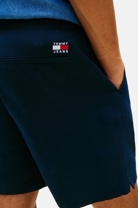 Short bleu de TOMMY JEANS, avec poche arrière et main dans la poche latérale.