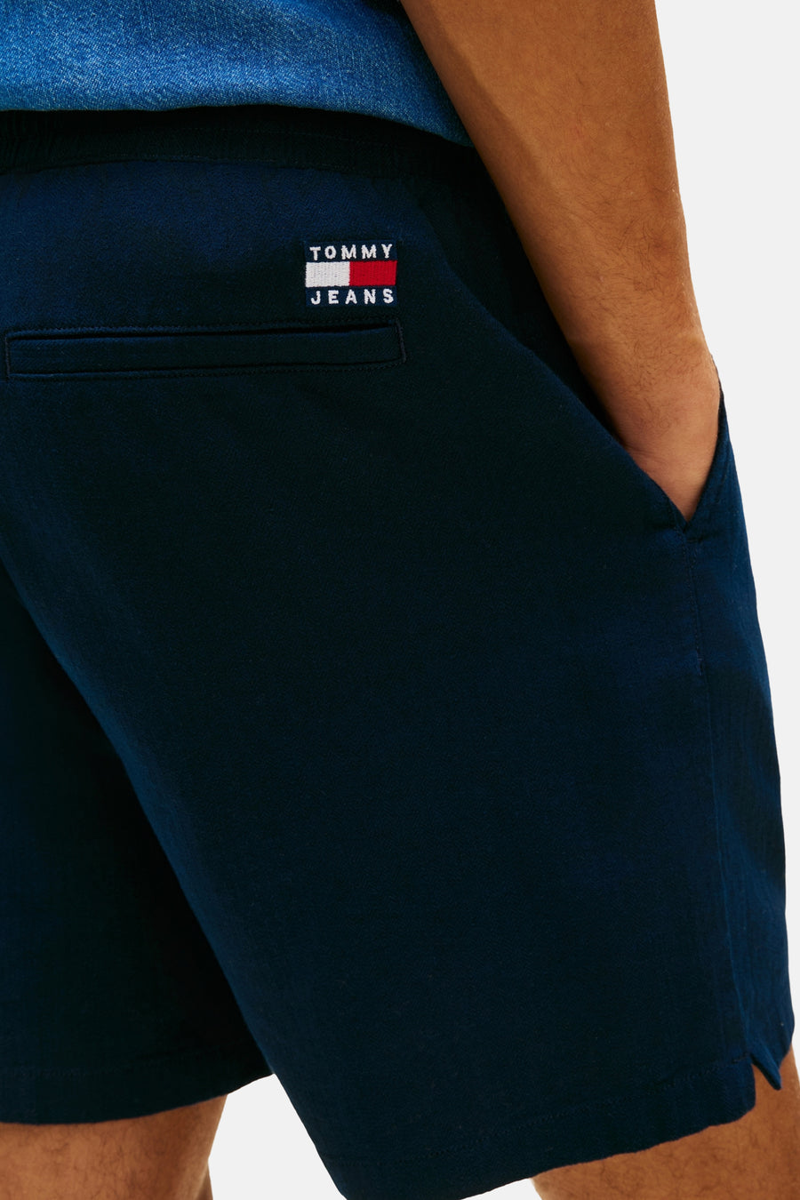 Short bleu de TOMMY JEANS, avec poche arrière et main dans la poche latérale.