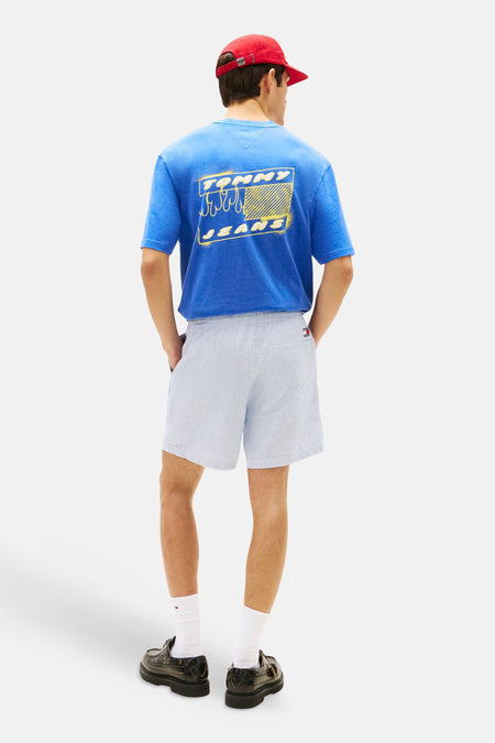 Short bleu TOMMY JEANS avec texture légère et étiquette logo, porté par un homme avec un t-shirt graphique.