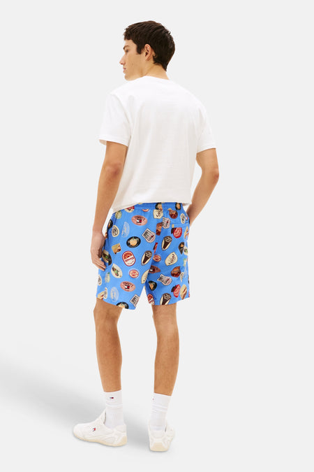 Short bleu de TOMMY JEANS avec un imprimé badge voyant, combiné avec un t-shirt blanc et des chaussettes blanches avec des baskets.