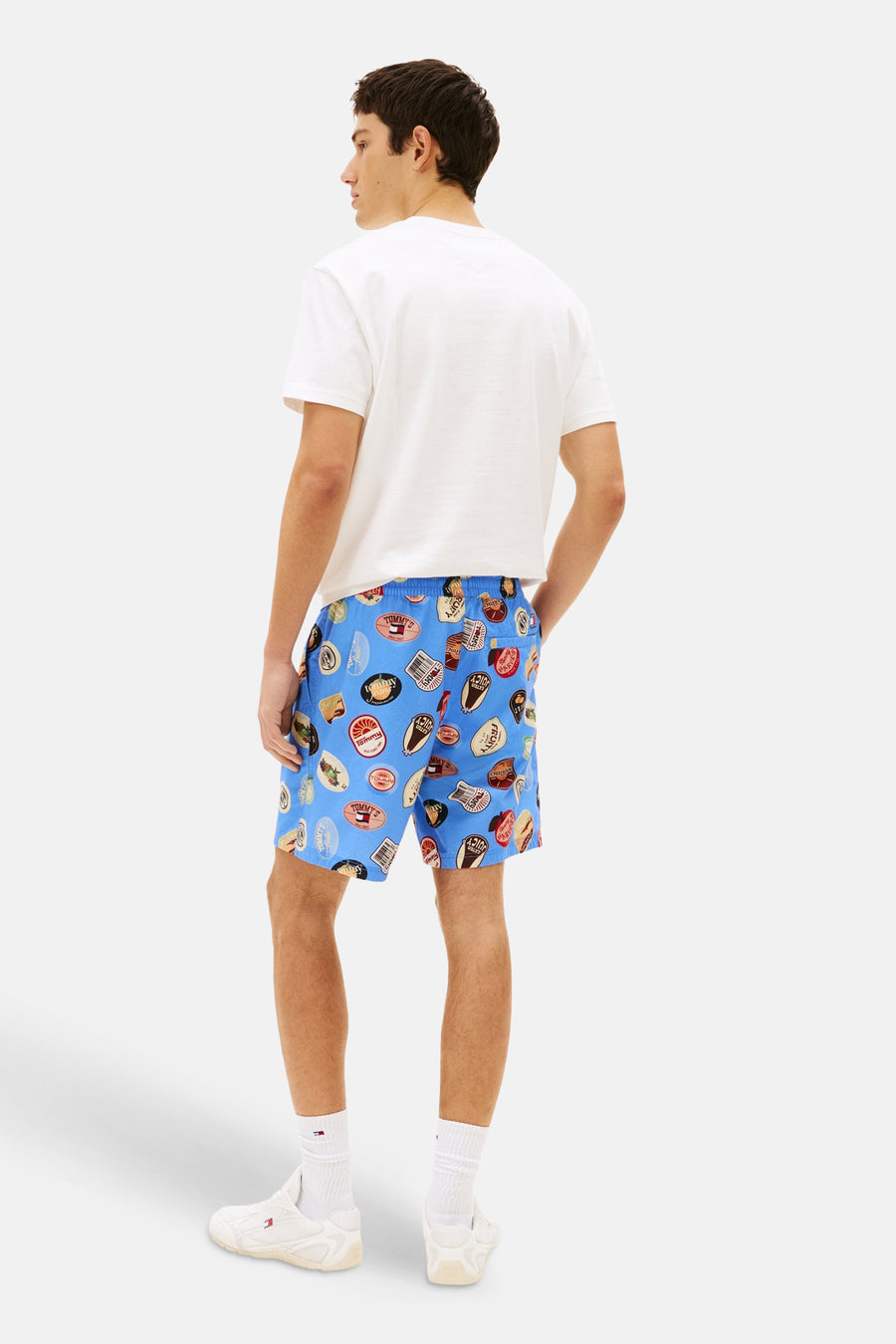Short bleu de TOMMY JEANS avec un imprimé badge voyant, combiné avec un t-shirt blanc et des chaussettes blanches avec des baskets.