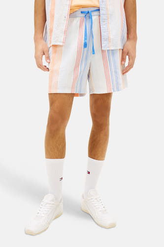 Short rayé multicolore de TOMMY JEANS, avec des rayures verticales en blanc, orange, bleu clair et rouge, porté en ensemble.