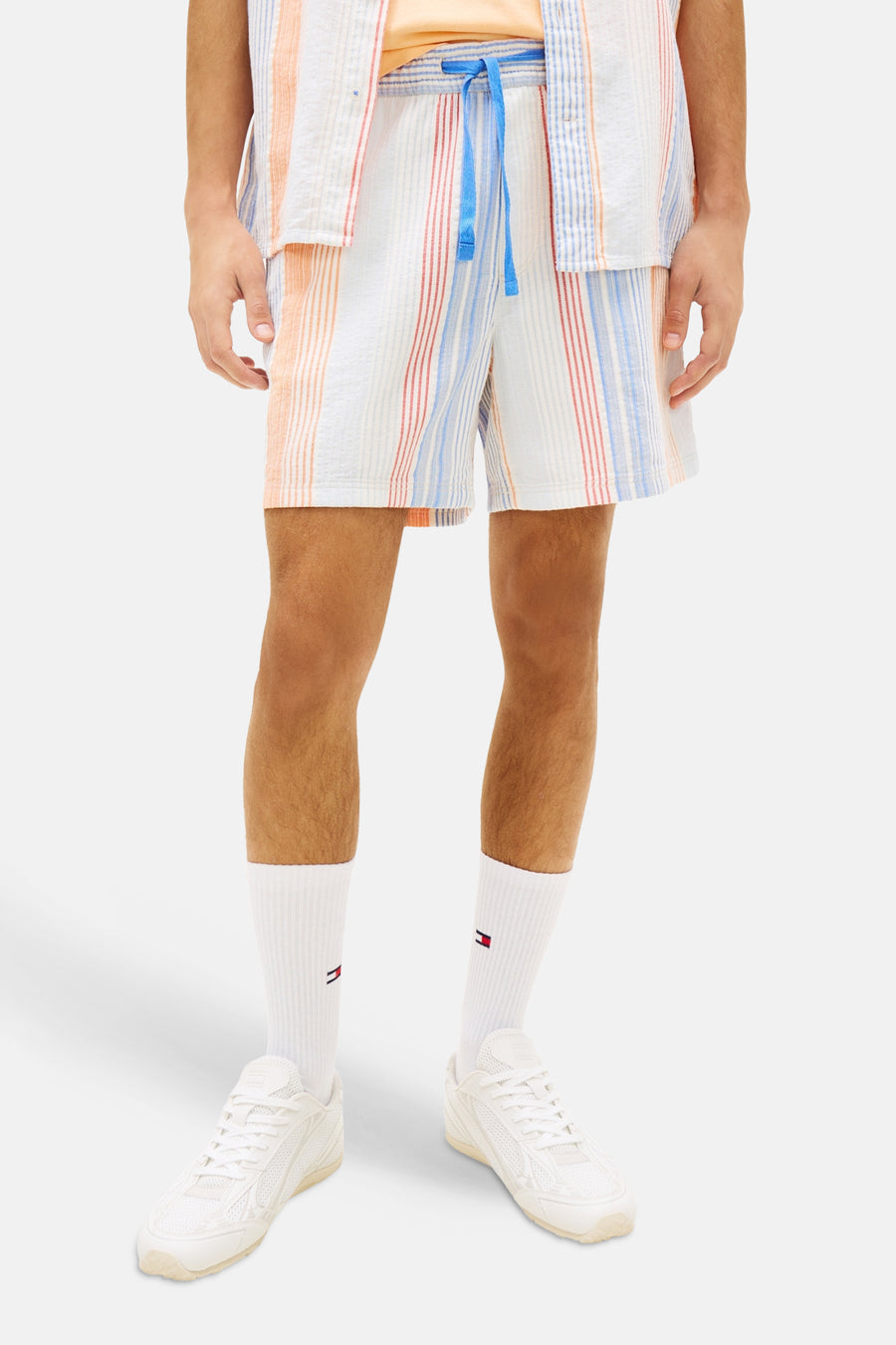 Short rayé multicolore de TOMMY JEANS, avec des rayures verticales en blanc, orange, bleu clair et rouge, porté en ensemble.