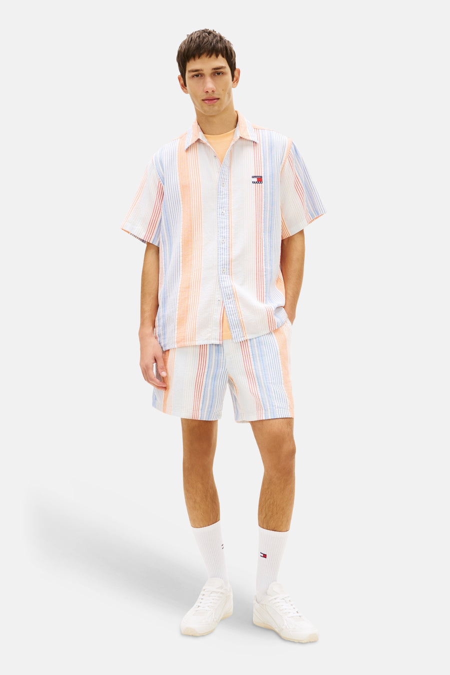 Veelkleurige gestreepte short van TOMMY JEANS, met verticale strepen in wit, oranje, lichtblauw en rood, gedragen als set.