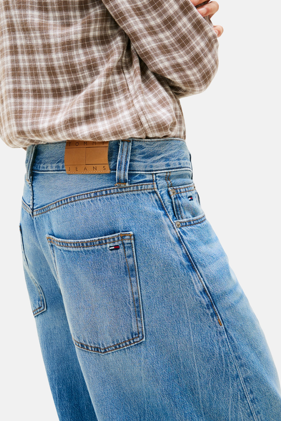 Jean bleu clair de TOMMY JEANS avec écusson logo en cuir marron sur la ceinture, combiné avec une chemise à carreaux.