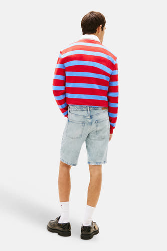 Short en jean bleu clair de TOMMY JEANS, vu de dos avec poches arrière visibles, porté par un homme avec une chemise à rayures rouges et bleues et des chaussures foncées.