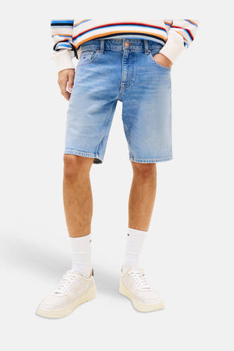 Short en jean de couleur bleu moyen de TOMMY JEANS, porté par un homme avec un pull rayé et des baskets blanches.