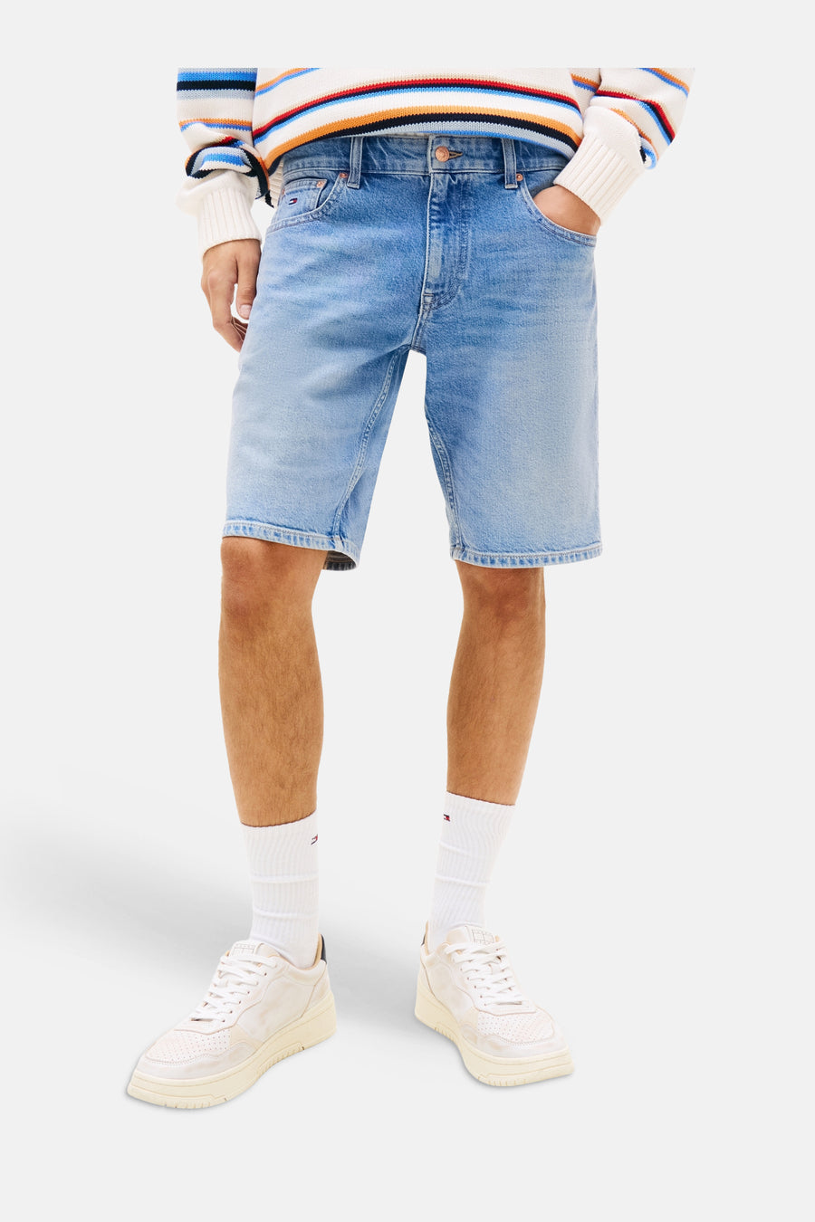 Short en jean de couleur bleu moyen de TOMMY JEANS, porté par un homme avec un pull rayé et des baskets blanches.