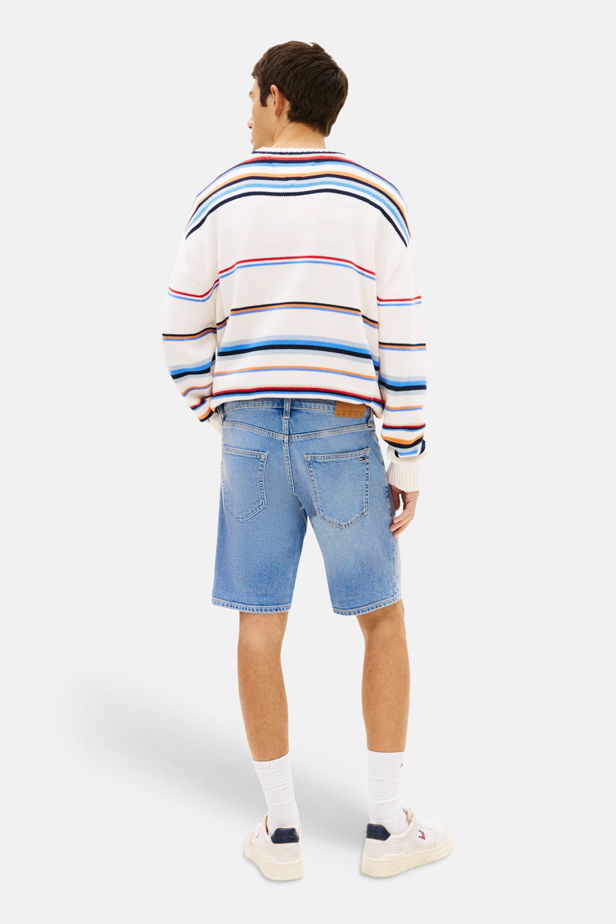 Short en jean de couleur bleu moyen de TOMMY JEANS avec poches arrière et écusson marron, porté par un homme en pull rayé.