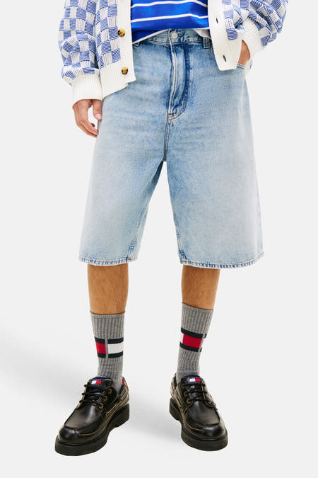 Short en jean en denim bleu moyen de TOMMY JEANS, avec jambes larges et poches apparentes, combiné avec un polo rayé et un cardigan en maille.