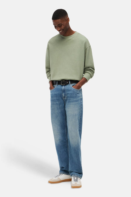 Pull vert avec col rond et texture gaufrée de TOMMY JEANS, porté par un homme en jean ample, ceinture noire et baskets.