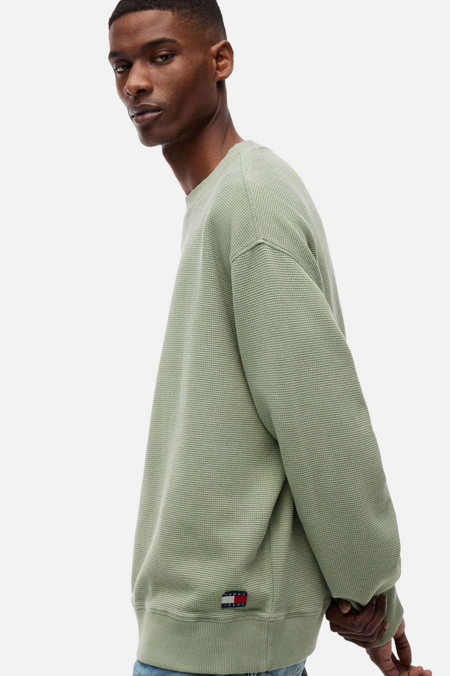 Groene sweater met ronde hals van TOMMY JEANS met wafelstructuur, logo op zoom en gedragen door een man.