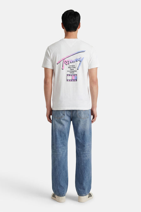 Witte korte mouwen T-shirt van TOMMY JEANS met kleurrijke achterprint en stedennamen, gezien van achteren op model in blauwe jeans