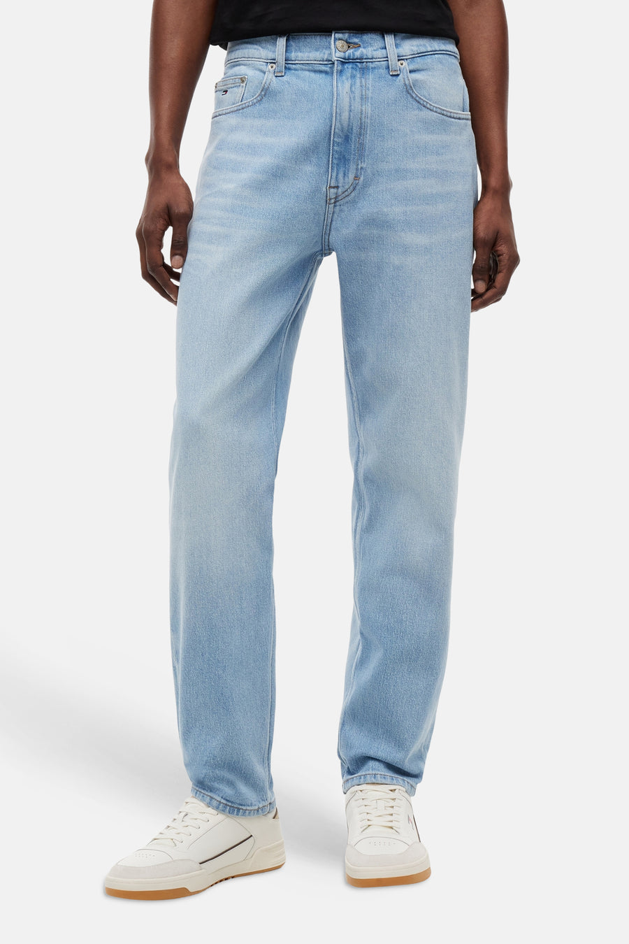Jean fuselé bleu clair de TOMMY JEANS, porté par un homme avec un t-shirt noir et des baskets blanches.