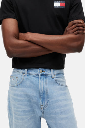 Jean slim fuselé bleu clair en denim de TOMMY JEANS, avec fermeture à boutons, poches avant et un petit logo drapeau sur la poche ticket, porté avec un t-shirt noir.