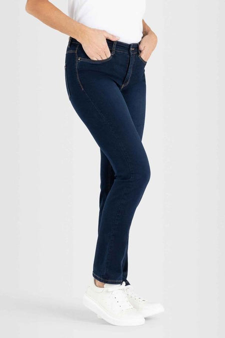 Donkerblauwe straight jeans van MAC, met zichtbare stiksels en gedragen met een witte top en sneakers.